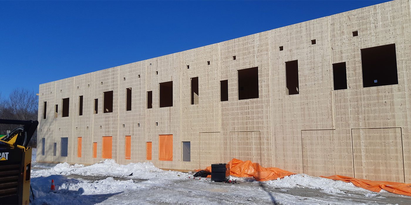 Long timber façade during construction with openings cut for windows